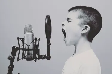 A boy with very short hair yelling into a microphone.