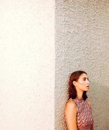 A woman leaning against a white wall looking despondent.