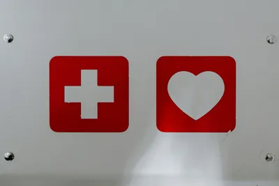 A white background with two red squares in the middle containing a white heart and cross.