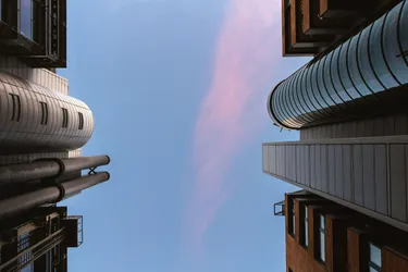 An view looking up at the sky as the sun sets surrounded by tall buildings.
