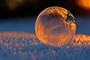 A drop of dew on snow reflecting the setting sun and sky above it