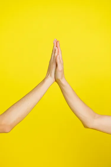 Two hands giving a high five with a yellow background.