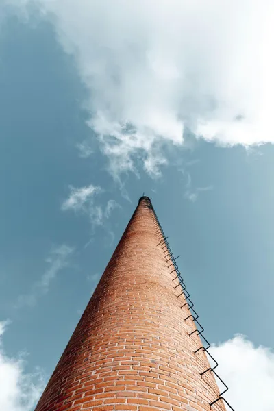 An old brick shot tower photographed from the bottom so that the towner appears to narrow dramatically as it points up to a sky with scattered clouds.