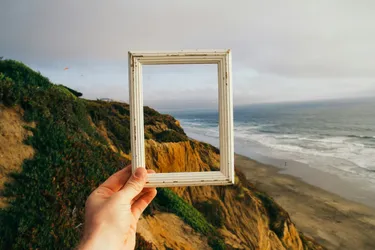 An empty picture frame being held to frame a cliff edge behind.