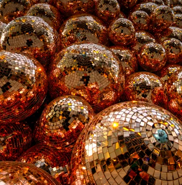 An image of hundreds of mirror balls in a pile, all reflecting an orange light.