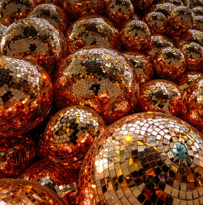 An image of hundreds of mirror balls in a pile, all reflecting an orange light.